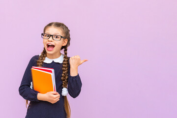 A schoolgirl holds notebooks and points to your advertisement on a pink isolated background....