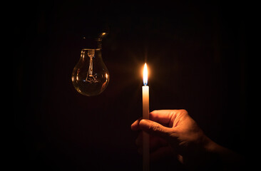 Hand holding a candle and an unlit lamp in the darkness. Lack of electricity