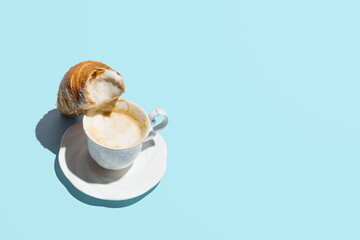 Vintage style cup of coffee with milk and fresh French croissant, perfect morning routine idea. Pastel blue background. 