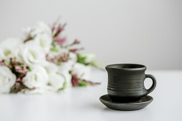 Black ceramic cup with coffee on table and bouquet of flowers.