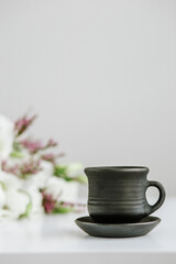Black ceramic cup with coffee on table and bouquet of flowers. Vertical.