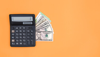 Calculator and dollar bills on an orange background, copy space.