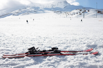 Mountain skis on bright alpine snow against the backdrop of mountains with ski slopes and ski lifts. Winter holidays. Extreme sport. Vacation, travel content. Copy space