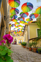 Fototapeta na wymiar Colorful fun umbrellas hanging over the street in Szentendre with flowers