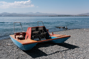 Old paddle boat (pedalo, water bike) on the pebble of Sevan lake beach on sunny summer day, Armenia.