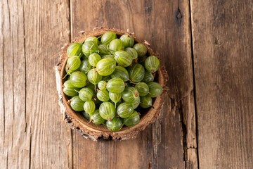 Green gooseberries in a wooden bowl. Harvest berries on a wooden table. Gooseberry summer vitamin food.