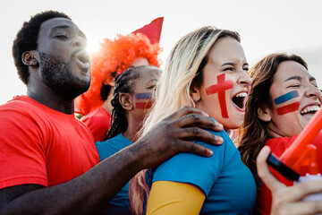 Multiracial red sport football fans celebrating with crowd cheering team on stadium tribune -...