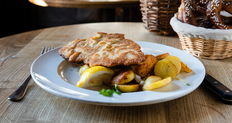 Wiener Schnitzel mit Bratkartoffeln und Preiselbeeren auf einem weißen Teller mit einer...