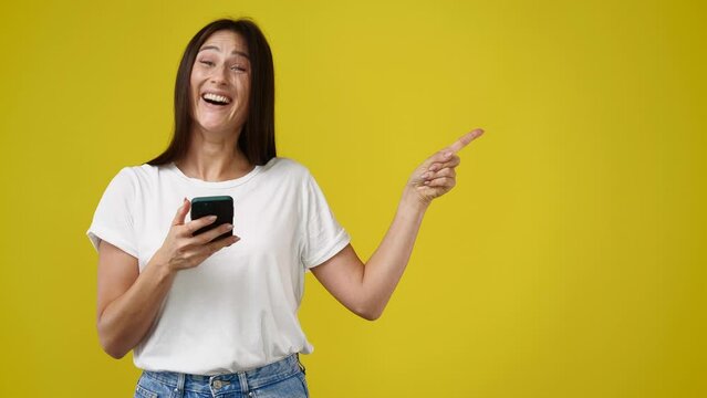 4k video of cute woman using phone and presentating something over yellow background.