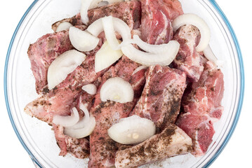 Close-up of pork bones with meat sprinkled with black pepper and onion slices in a glass bowl.