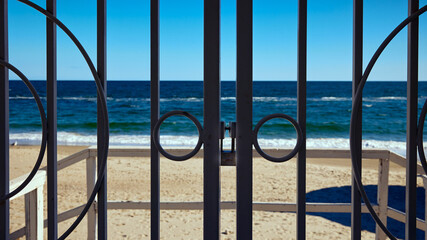 A gate with a lock closes the entrance to the beach with blue sea and sky in the background