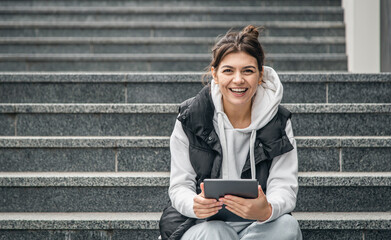 A young female student stands with a digital tablet in her hands outside.