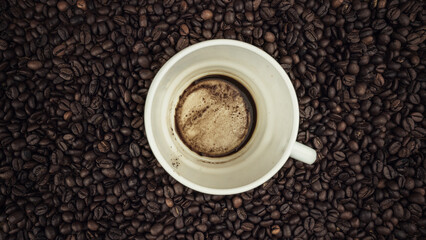 Empty dirty white cup with coffee remains over roasted beans background