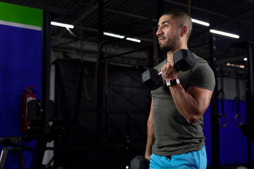latino man with sportswear doing biceps exercises with two dumbbells in a gym