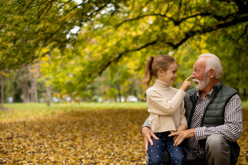 Fototapeta premium Grandfather spending time with his granddaughter in park on autumn day