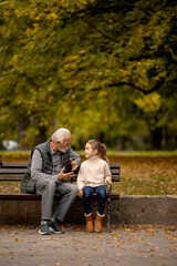 Naklejka na ściany i meble Grandfather spending time with his granddaughter on bench in park on autumn day