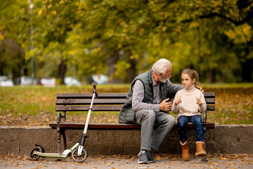Grandfather spending time with his granddaughter on bench in park on autumn day