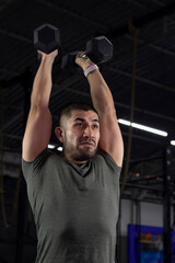 Fototapeta na wymiar Mexican man in sportswear exercising in a gym using two dumbbells