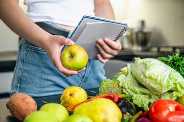 Woman with notepad and vegetables on the kitchen table preparing a recipe.