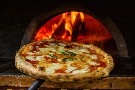 Pizza Margherita napoletana con sugo di pomodoro, mozzarella e basilico appena uscita dal forno a legna sullo sfondo