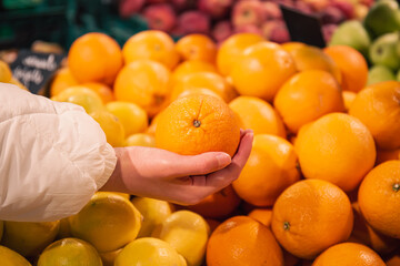 Close-up, woman choosing orange at the grocery store.