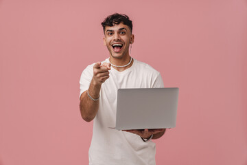 Young handsome enthusiastic man holding laptop and looking at camera