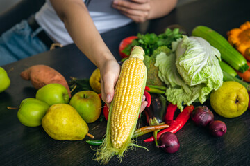 Close-up, corn in female hands and other vegetables on the kitchen table.