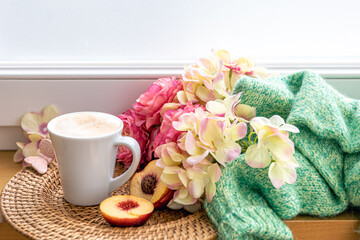 Home composition with a cup of coffee, flowers and a knitted element.