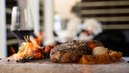 Delicious steak on the salt stone with grilled vegetables, potato and sous. Restaurant background,...