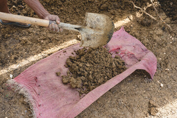 A man shovels some dirt into a a sack for carrying. Digging a hole for a house foundation.