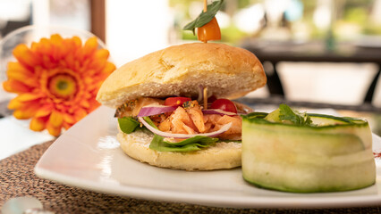 Tasty burger with salmon, tomatoes, onions and fresh salad. Restaurant in the background. Healthy food
