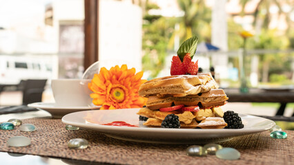 Beautiful served dessert. Waffles with strawberries and blackberries Gerbera flower and restaurant background