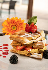 Beautiful served dessert. Waffles with strawberries and blackberries Gerbera flower and restaurant background