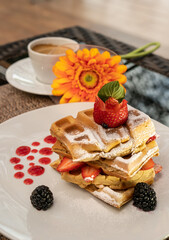 Beautiful served dessert. Waffles with strawberries and blackberries Gerbera flower and restaurant background