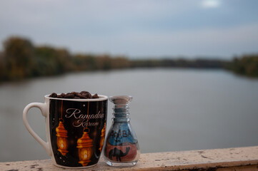 Cup of coffee and bottle with sand next to river