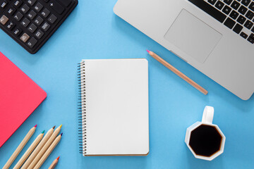 Flat lay, notepad, laptop and stationery on blue background.