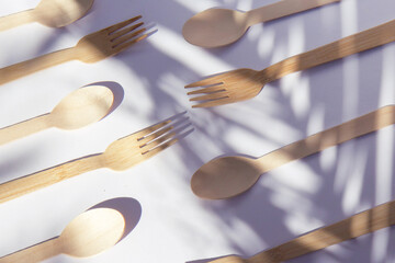 Wooden eco bamboo cutlery forks on bright white background with contrasting shadows from palm leaves. Meal time concept