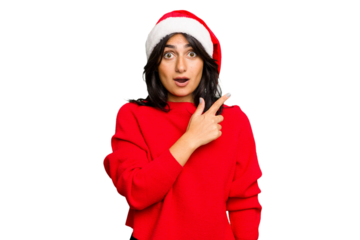 Young Indian woman celebrating Christmas wearing a santa hat isolated pointing to the side
