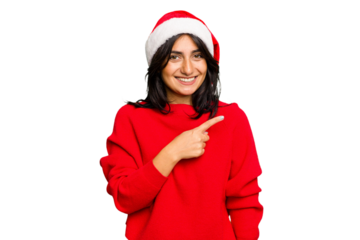 Young Indian woman celebrating Christmas wearing a santa hat isolated smiling and pointing aside, showing something at blank space.