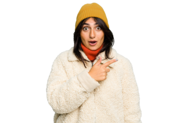 Young Indian woman wearing winter jacket and a wool cap isolated pointing to the side