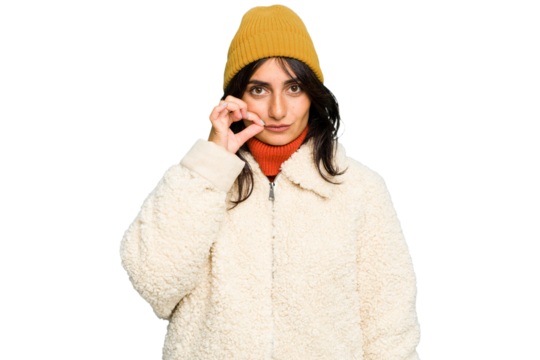 Young Indian woman wearing winter jacket and a wool cap isolated with fingers on lips keeping a secret.