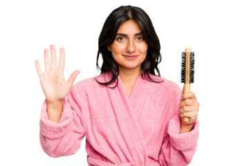 Young Indian woman in a bathrobe holding an hairbrush isolated smiling cheerful showing number five with fingers.
