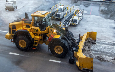 A bulldozer shovels snow from a snowy runway