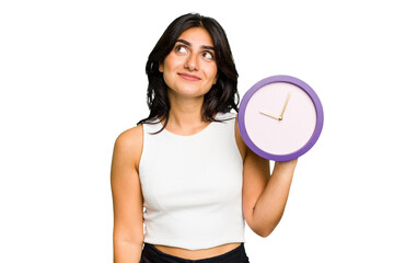 Young Indian woman holding a clock isolated dreaming of achieving goals and purposes