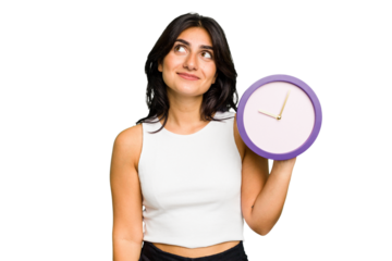 Young Indian woman holding a clock isolated dreaming of achieving goals and purposes