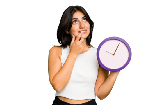 Young Indian woman holding a clock isolated relaxed thinking about something looking at a copy space.