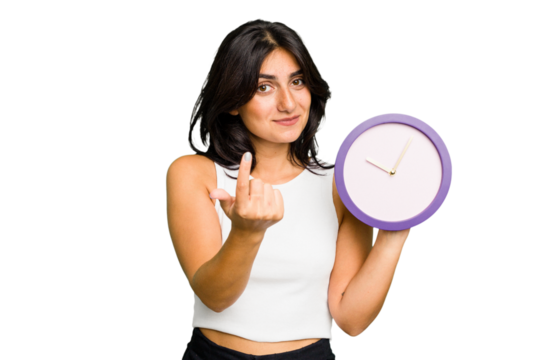 Young Indian woman holding a clock isolated pointing with finger at you as if inviting come closer.