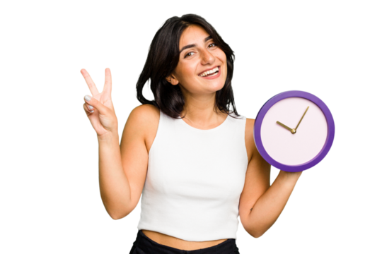 Young Indian woman holding a clock isolated joyful and carefree showing a peace symbol with fingers.