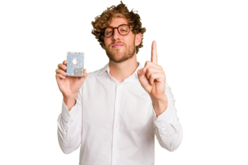 Young caucasian informatic man holding a hard drive isolated on white background showing number one with finger.