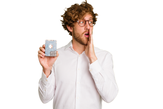 Young caucasian informatic man holding a hard drive isolated on white background is saying a secret hot braking news and looking aside